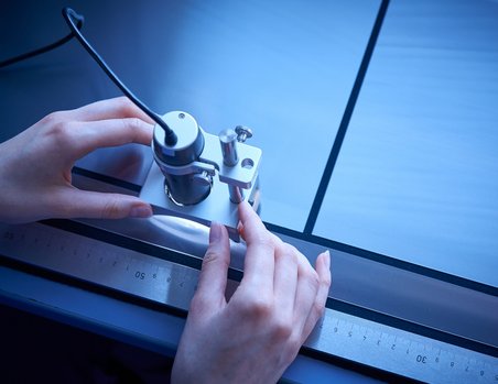 Ein Paar Hände schneidet an einem Arbeitstisch mit einem elektronischen Schneidgerät und Lineal Folien zurecht.