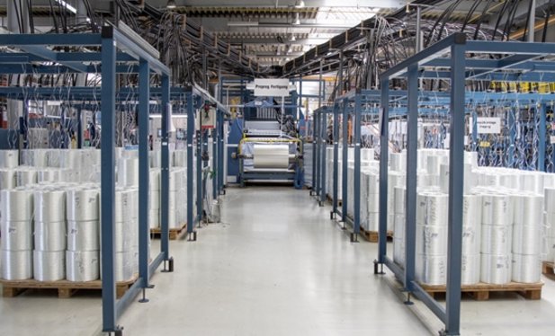 In einer Fabrikhalle sind recht und links eines Ganges mehrere Materialrollen übereinander gelagert.