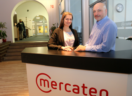Zwei Mercateo Mitarbeiter stehen hinter einem Tresen mit der Firmenaufschrift in den Geschäftsräumen des Unternehmens.