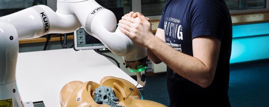 Ein Mann steht an einem OP-Roboter, der die künstliche Wirbelsäule einer Übungspuppe operiert.