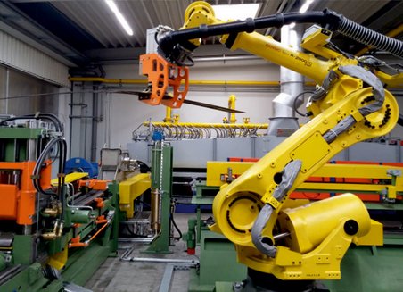 Maschinenbetriebener Roboterarm transportiert ein Bauteil von einer Maschine zu einer anderen.